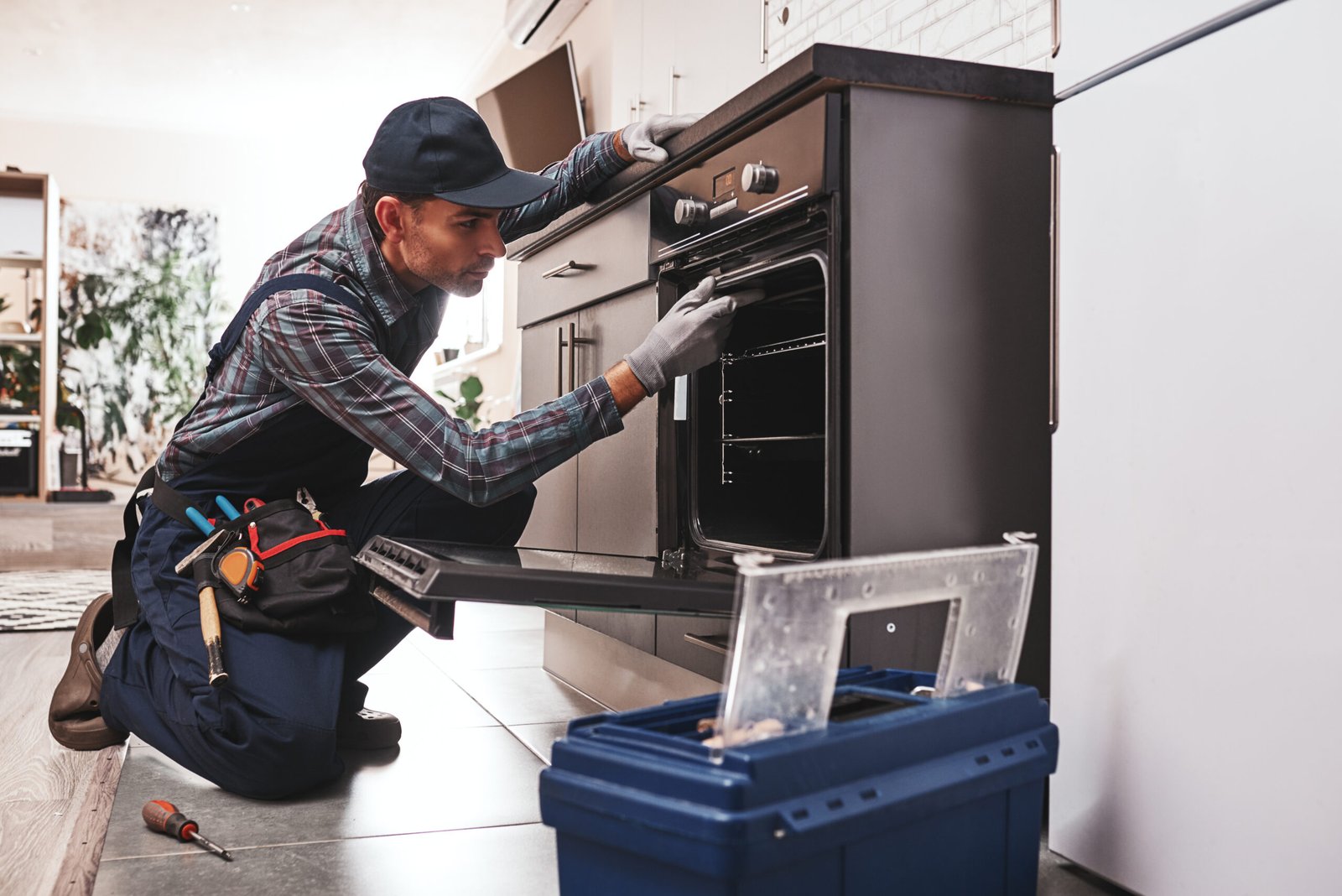 Don't delay with repair. Close-up of repairman examining oven with screwdriver in kitchen with tool case
