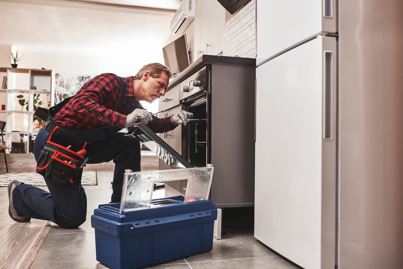 Whats up with oven. Full length of repairman examining oven with flashlight in kitchen with tool case