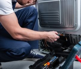 partial view of repairman in working overall fixing refrigerator by screwdriver in kitchen
